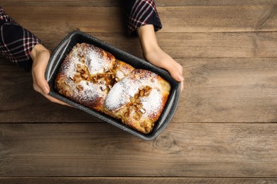 Woman holding baking pan with delicious yeast dough cake at wooden table, top view