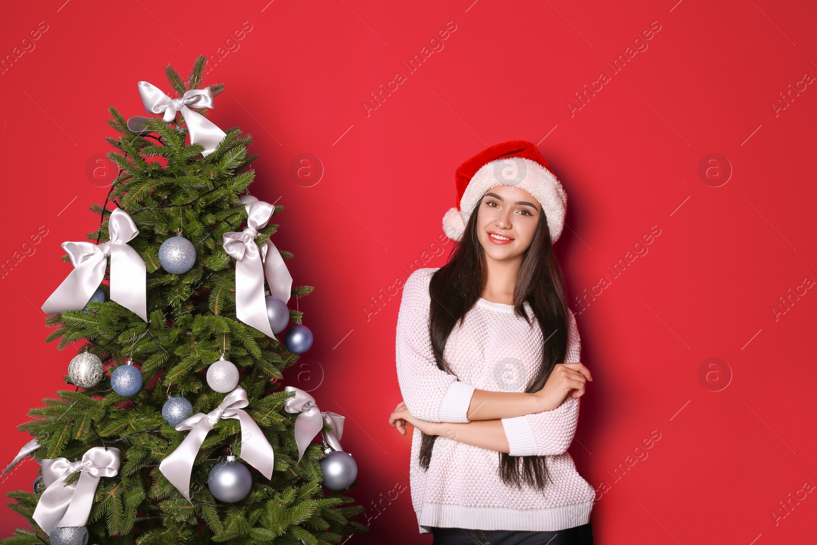 Photo of Beautiful young woman in Santa hat near Christmas tree on color background