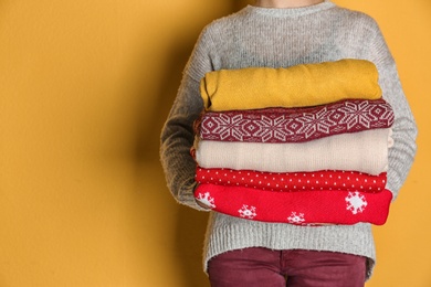 Photo of Woman holding stack of winter clothes on color background. Space for text