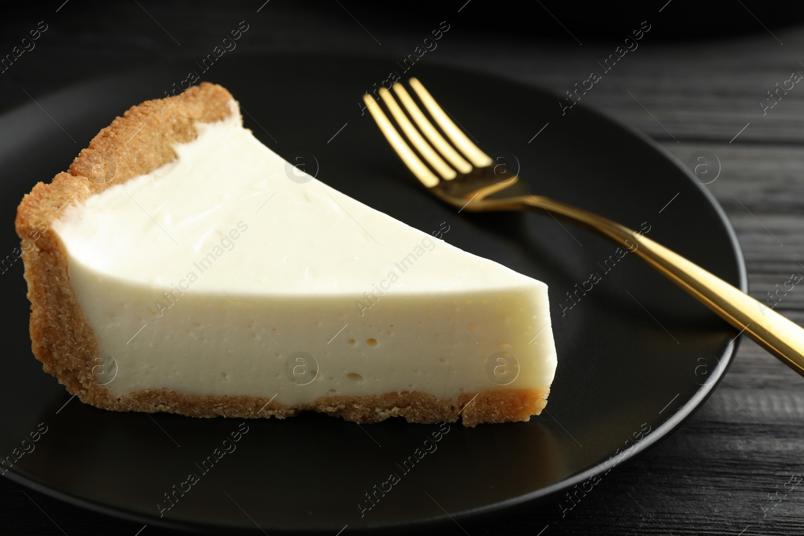 Photo of Piece of tasty vegan tofu cheesecake and fork on black wooden table, closeup