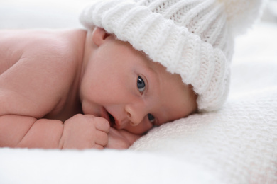 Photo of Cute newborn baby in white knitted hat on plaid, closeup