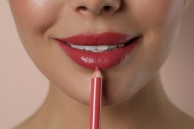 Photo of Young woman applying beautiful pink lip pencil on light background, closeup