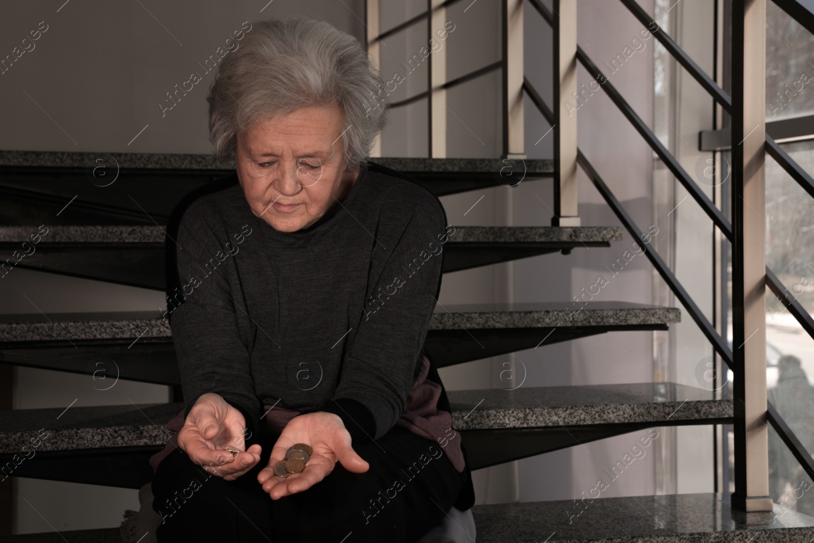 Photo of Poor upset mature woman with coins on stairs. Space for text