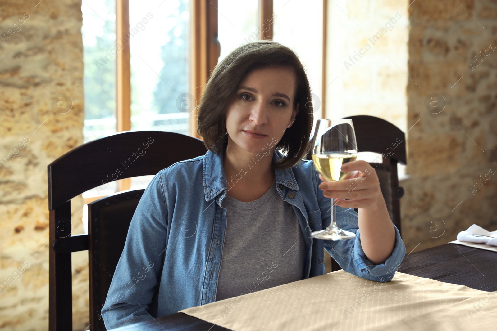 Photo of Woman with glass of white wine at table indoors