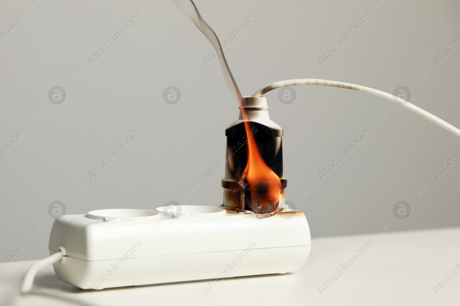 Photo of Inflamed plug in power strip on white table against grey wall. Electrical short circuit