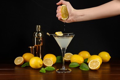 Photo of Woman squeezing lemon into Martini cocktail at wooden table, closeup