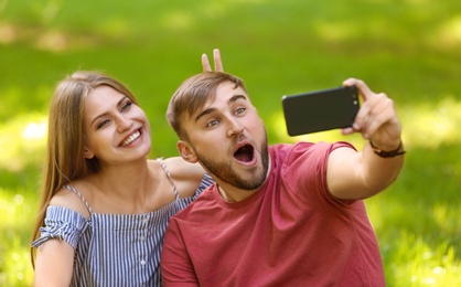 Happy young couple taking selfie on green grass in park