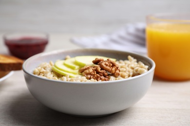 Photo of Tasty oatmeal porridge with walnuts and apple slices on white wooden table, closeup