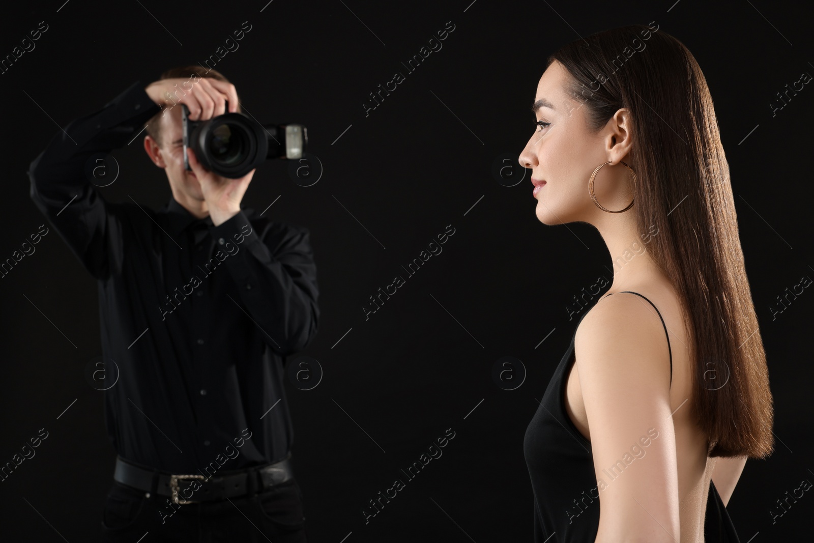 Photo of Professional photographer taking picture of beautiful young woman on black background, selective focus