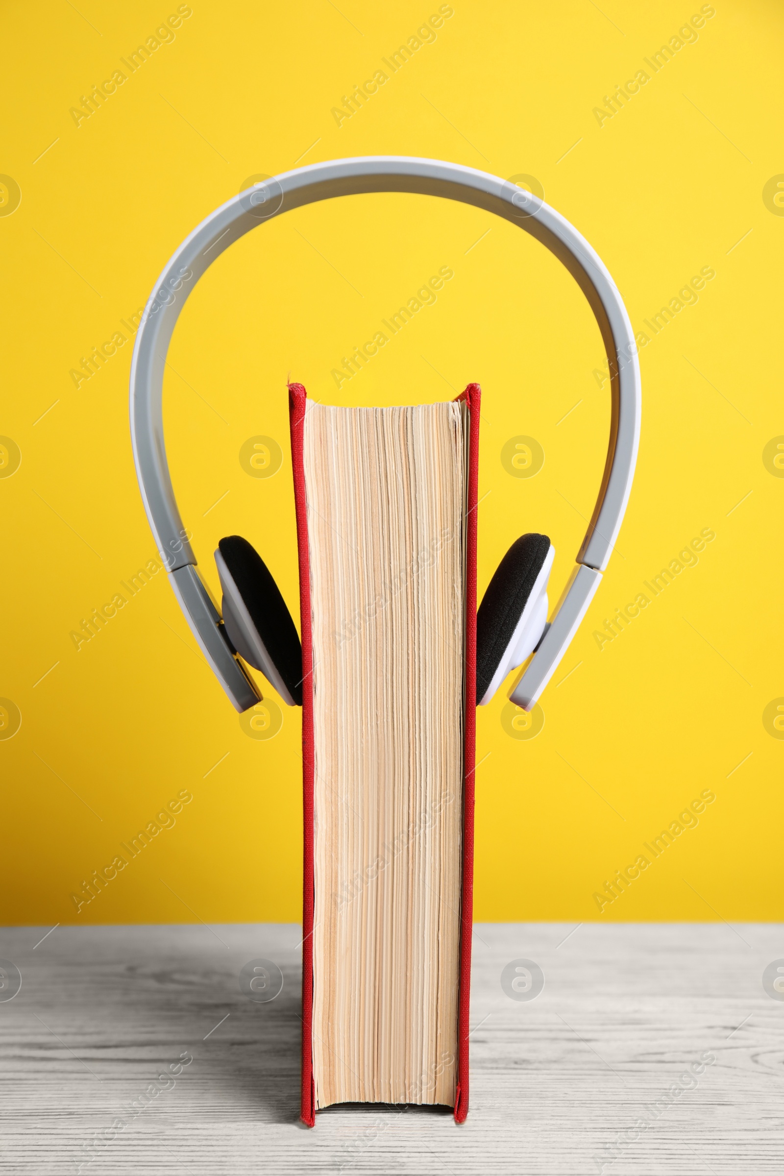 Photo of Book and modern headphones on white wooden table against yellow background