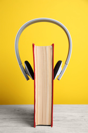 Book and modern headphones on white wooden table against yellow background