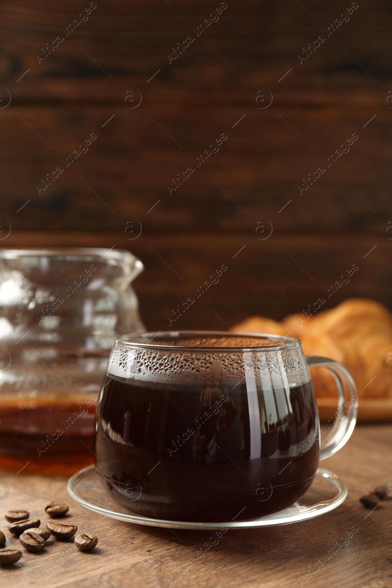 Photo of Hot coffee in glass cup and beans on wooden table, closeup. Space for text