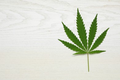 Photo of Fresh green hemp leaf on white wooden table, top view. Space for text