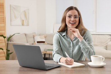 Happy woman with notebook and laptop at wooden table in room