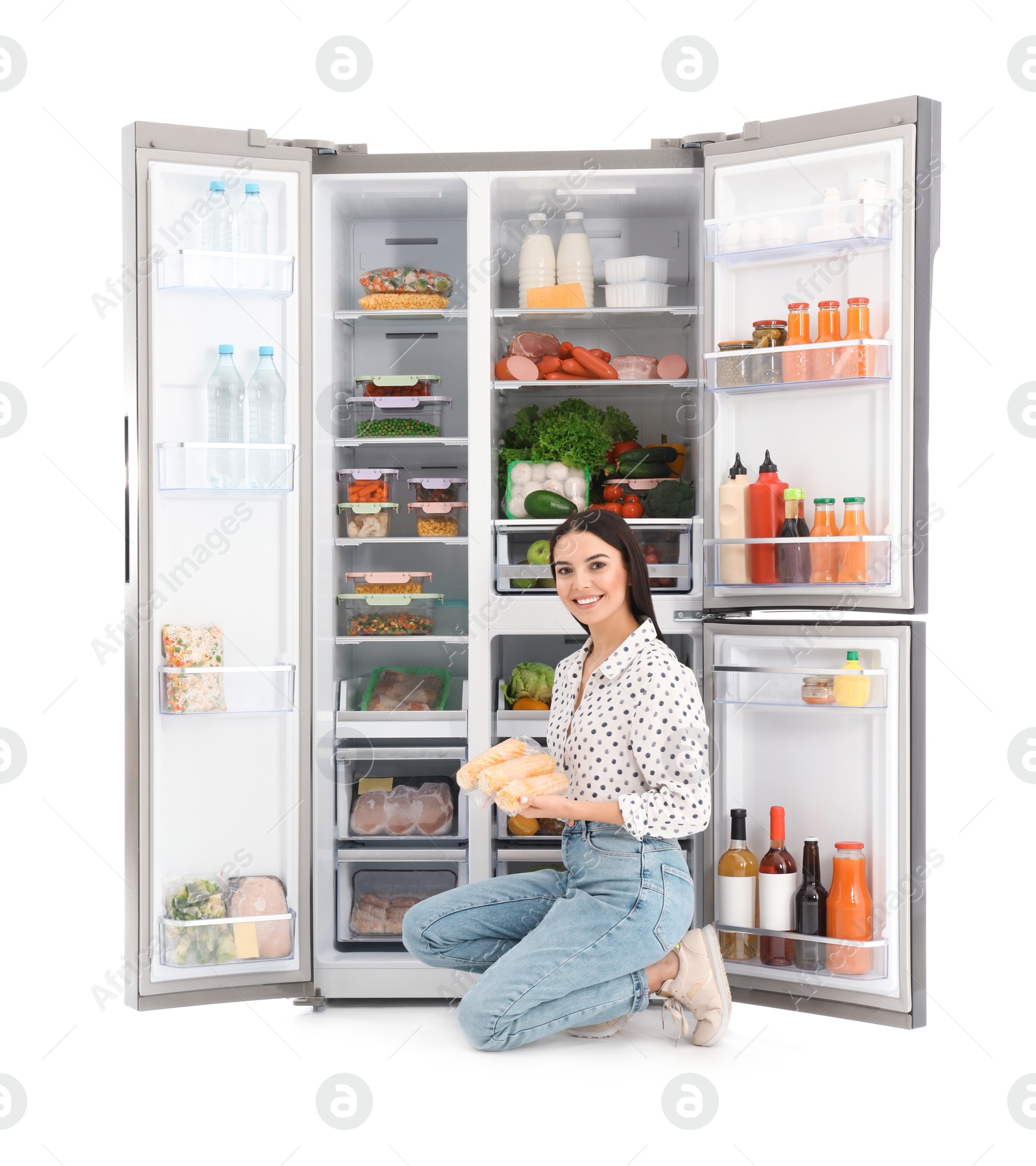 Photo of Young woman with corn near open refrigerator on white background