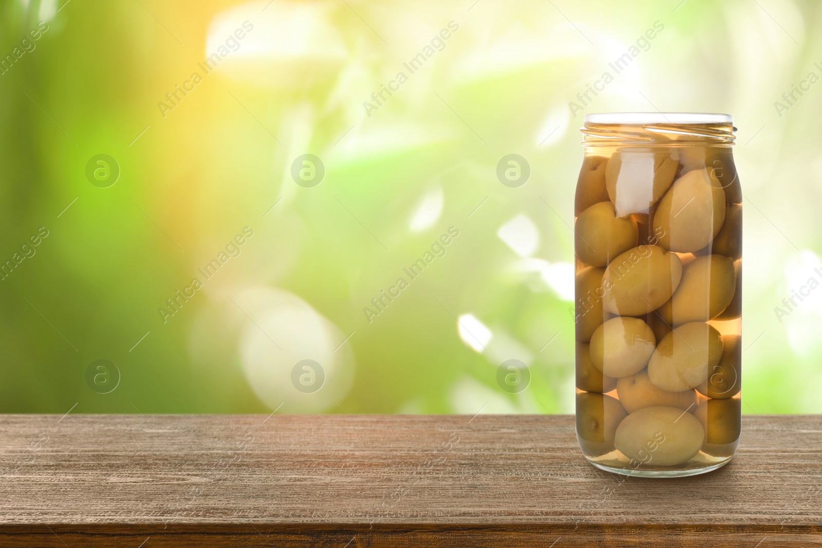 Image of Jar of pickled olives on wooden table against blurred background, space for text