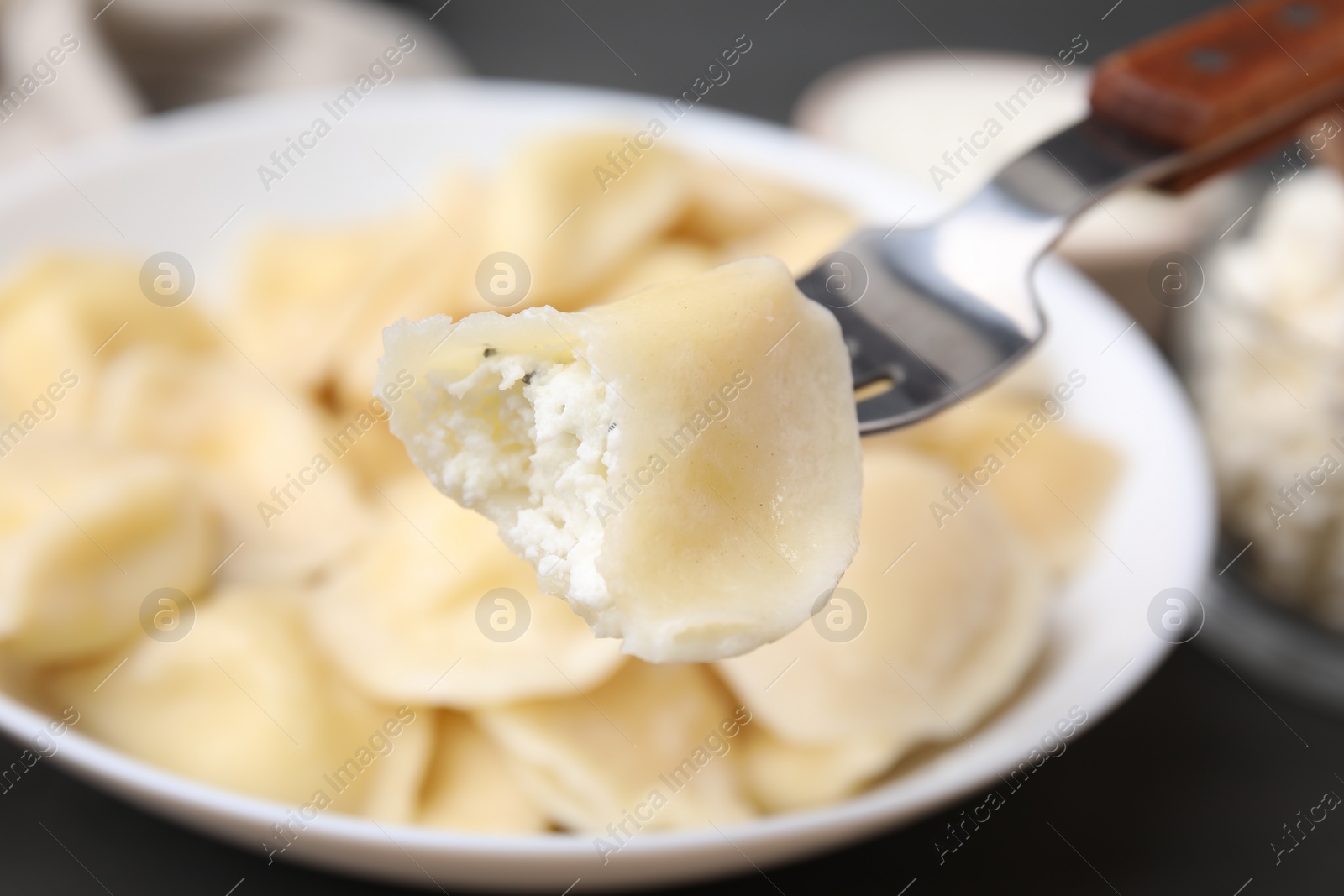 Photo of Delicious dumpling (varenyk) with cottage cheese on fork over bowl, closeup