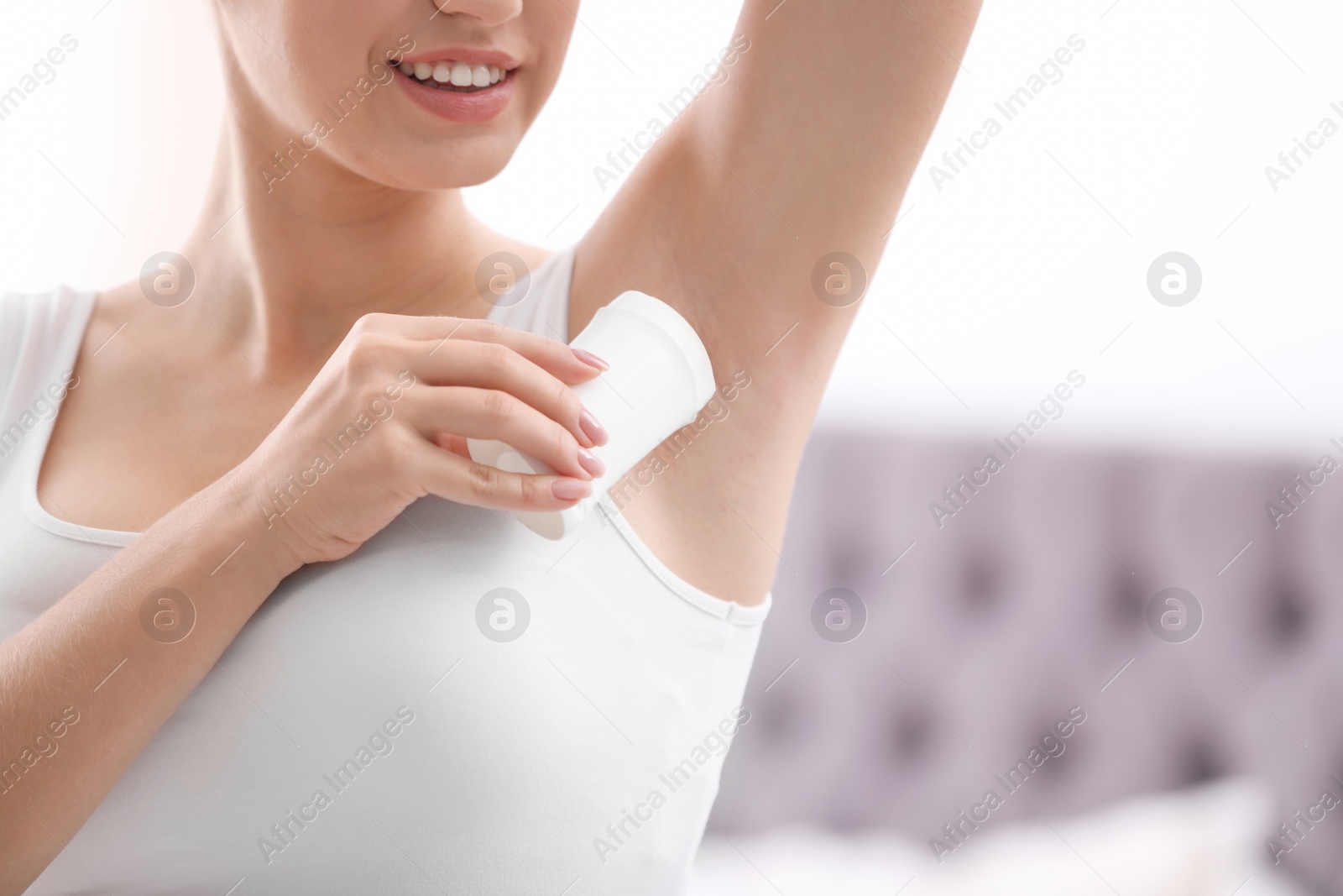 Photo of Beautiful young woman applying deodorant in bedroom. Space for text