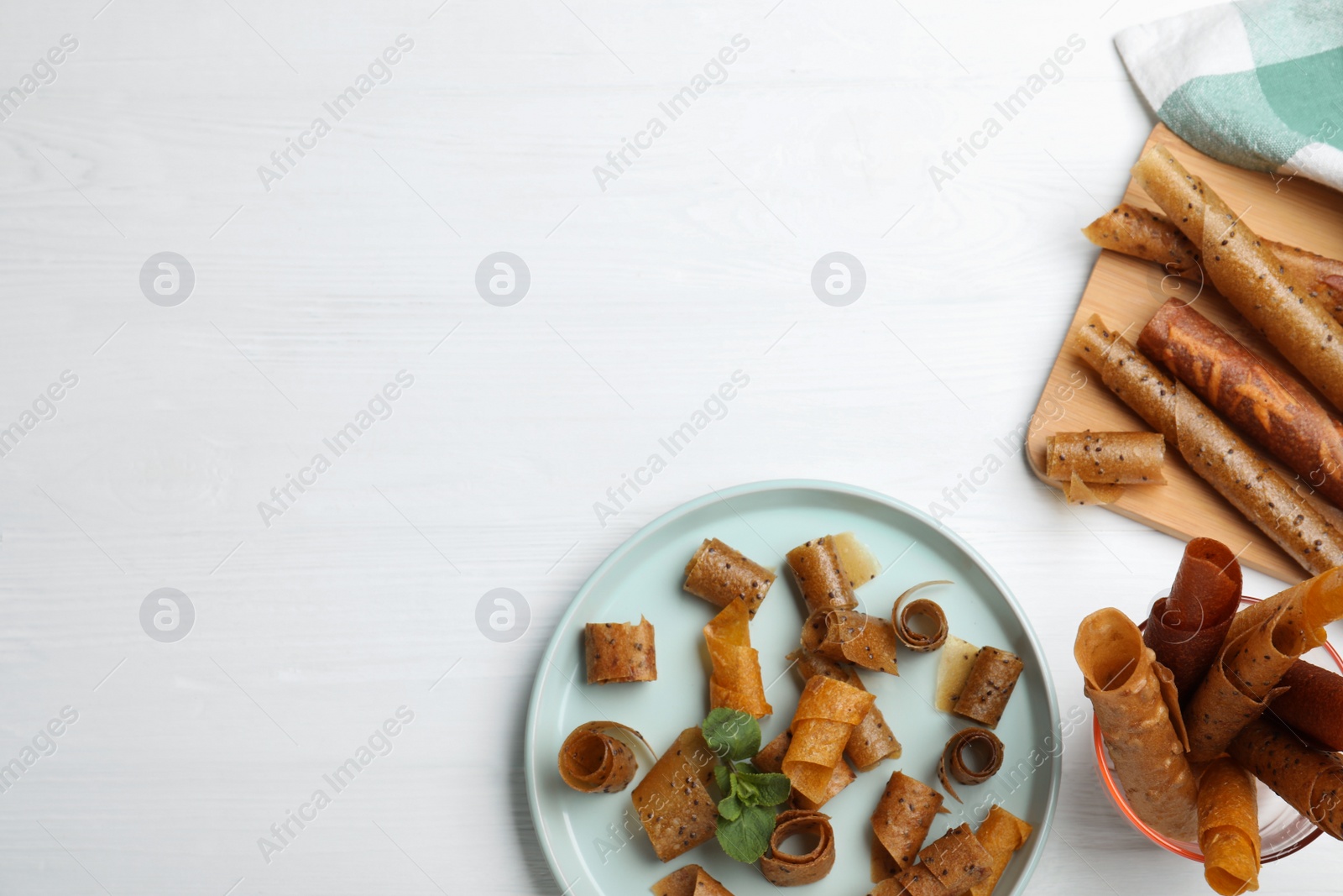 Photo of Delicious fruit leather rolls on white wooden table, flat lay. Space for text