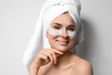 Photo of Beautiful woman with eye patches against light background. Facial mask