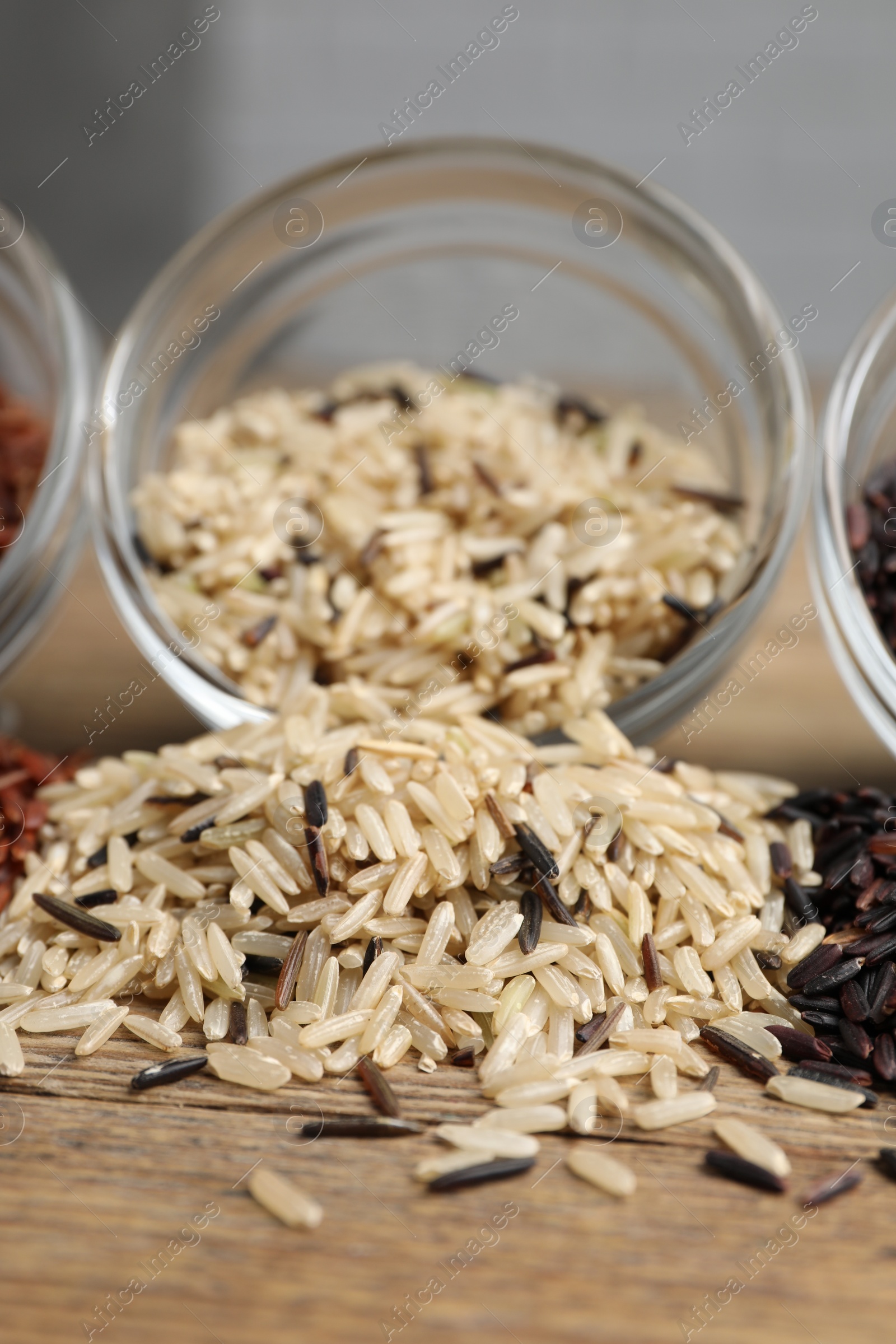 Photo of Glass bowl of raw unpolished rice on wooden table, closeup