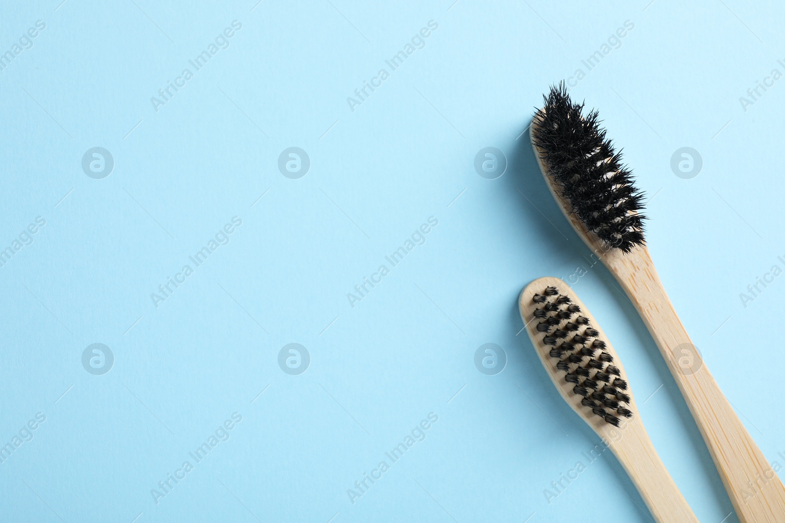 Photo of Two bamboo toothbrushes on light blue background, flat lay. Space for text