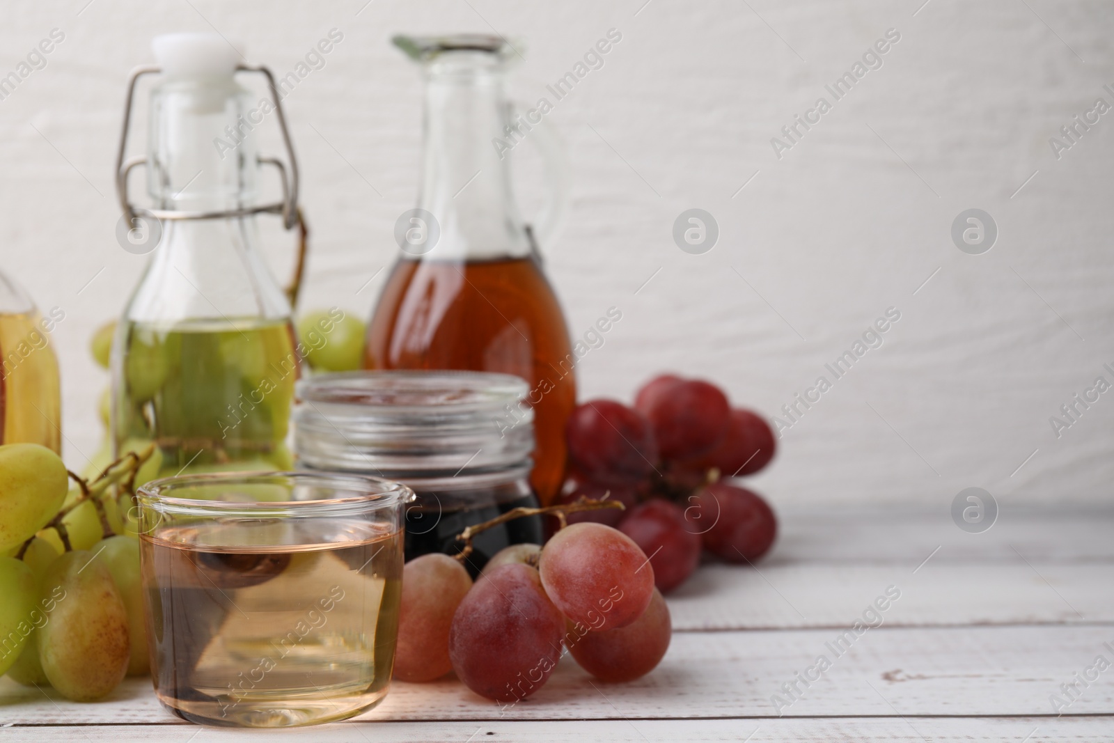 Photo of Different types of vinegar and grapes on wooden table, closeup. Space for text