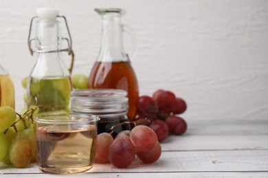 Different types of vinegar and grapes on wooden table, closeup. Space for text