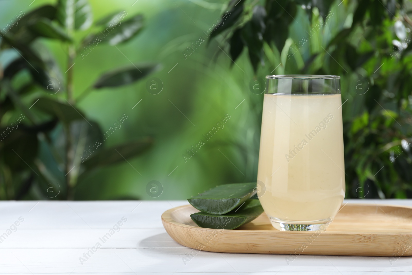 Photo of Fresh aloe juice in glass and cut leaves on white wooden table outdoors, space for text