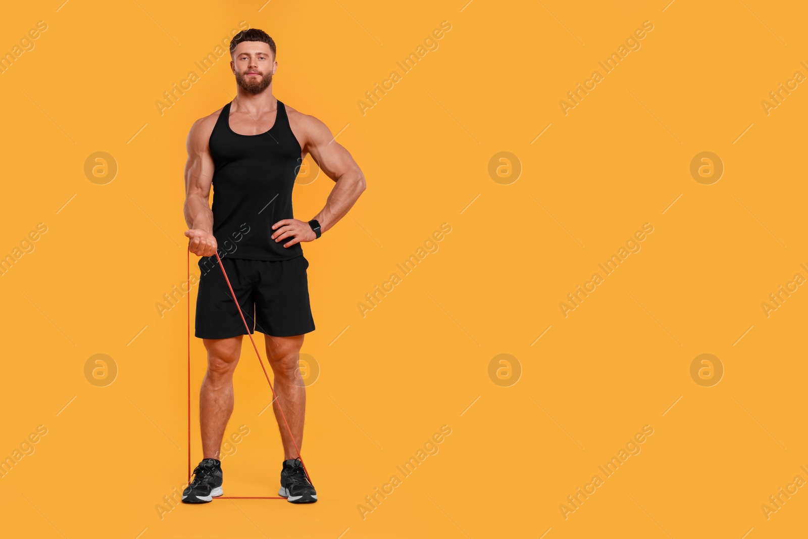 Photo of Young man exercising with elastic resistance band on orange background. Space for text