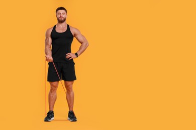 Young man exercising with elastic resistance band on orange background. Space for text