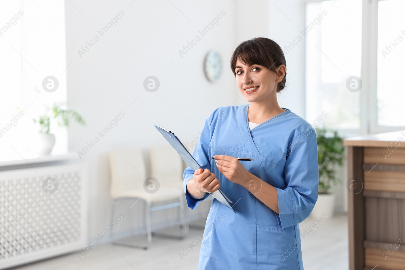 Photo of Portrait of smiling medical assistant with clipboard in hospital. Space for text