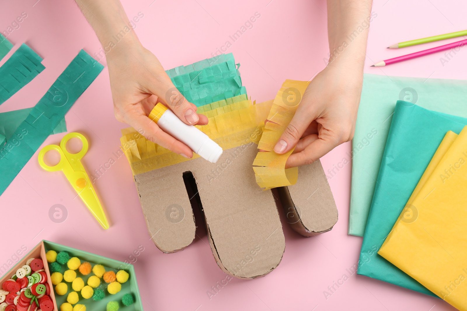 Photo of Woman decorating cardboard cactus at pink background, top view. Pinata DIY