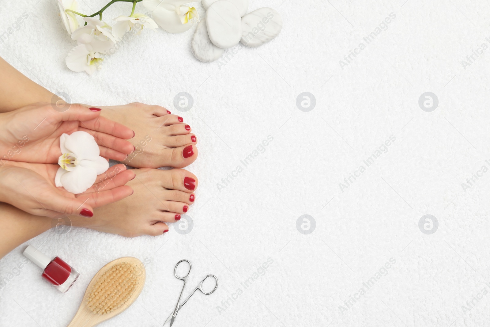 Photo of Woman with stylish red toenails after pedicure procedure and orchid flowers on white terry towel, top view. Space for text