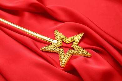 Photo of Beautiful golden magic wand on red fabric, closeup