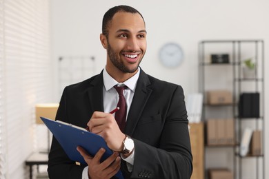 Photo of Smiling young man with clipboard writing notes in office. Lawyer, businessman, accountant or manager