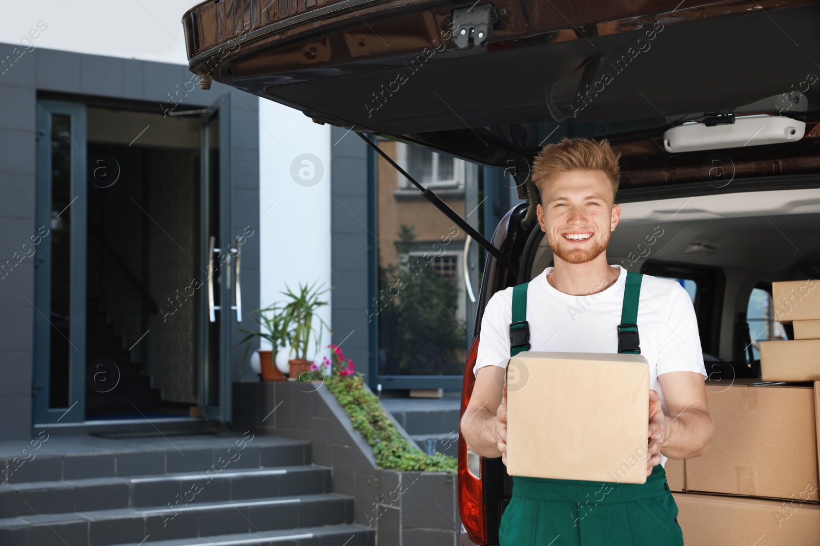 Photo of Young courier with parcel near delivery car outdoors. Space for text