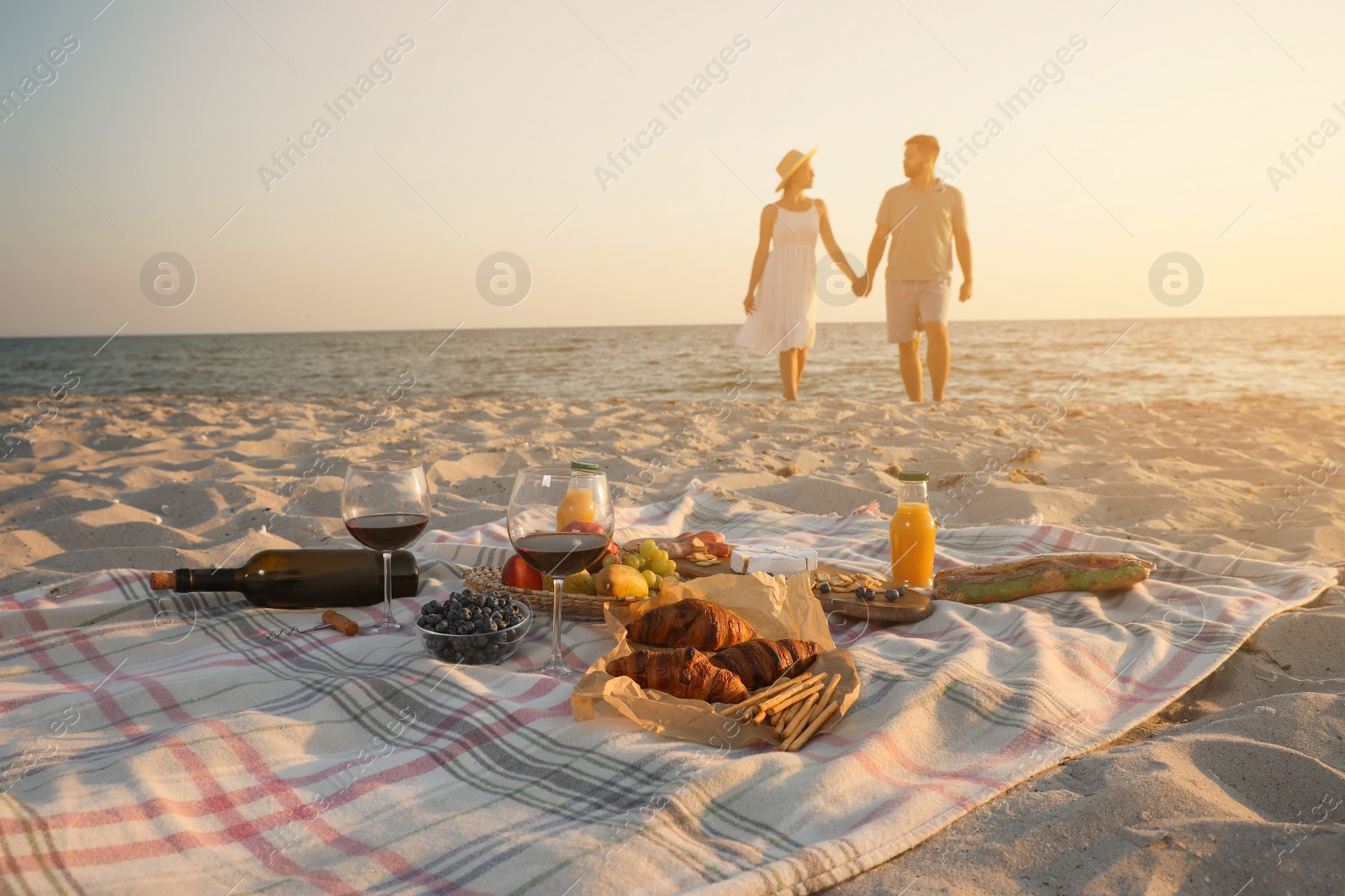 Photo of Couple walking by sea, focus on blanket with food and snacks. Summer picnic