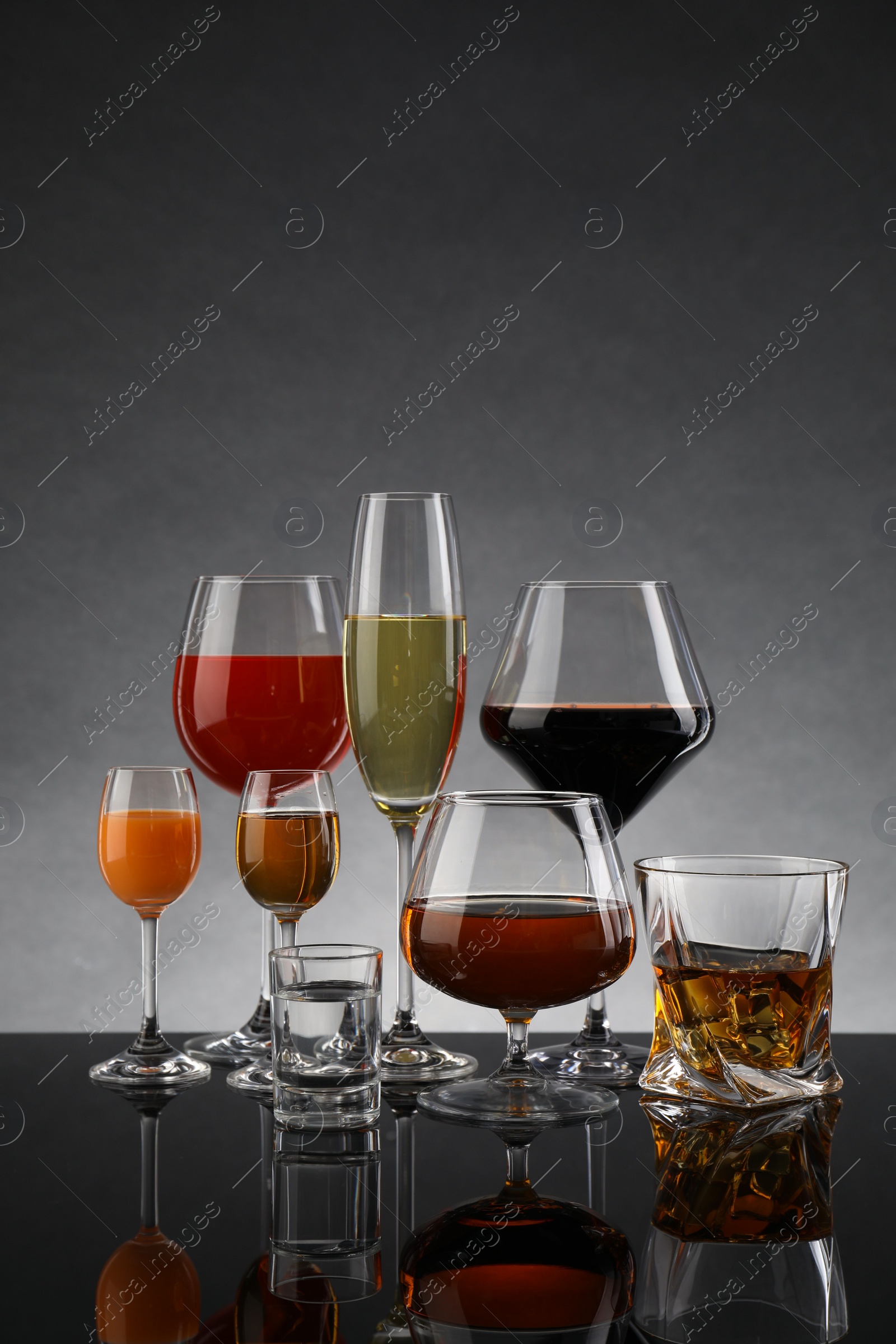 Photo of Glasses with different alcoholic drinks on table against gray background