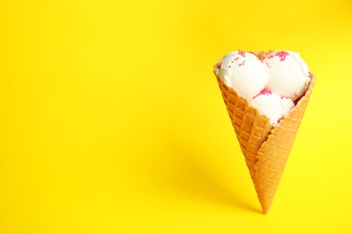 Photo of Delicious vanilla ice cream in wafer cone on yellow background. Space for text