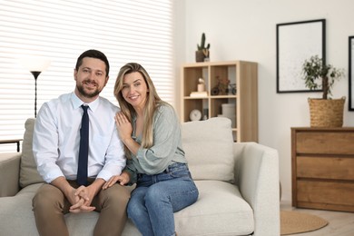 Photo of Happy couple sitting on sofa at home, space for text