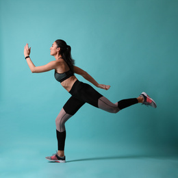 Photo of Athletic young woman running on turquoise background, side view