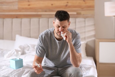 Photo of Ill man with nasal spray and paper tissue on bed at home