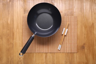 Empty iron wok and chopsticks on wooden table, top view