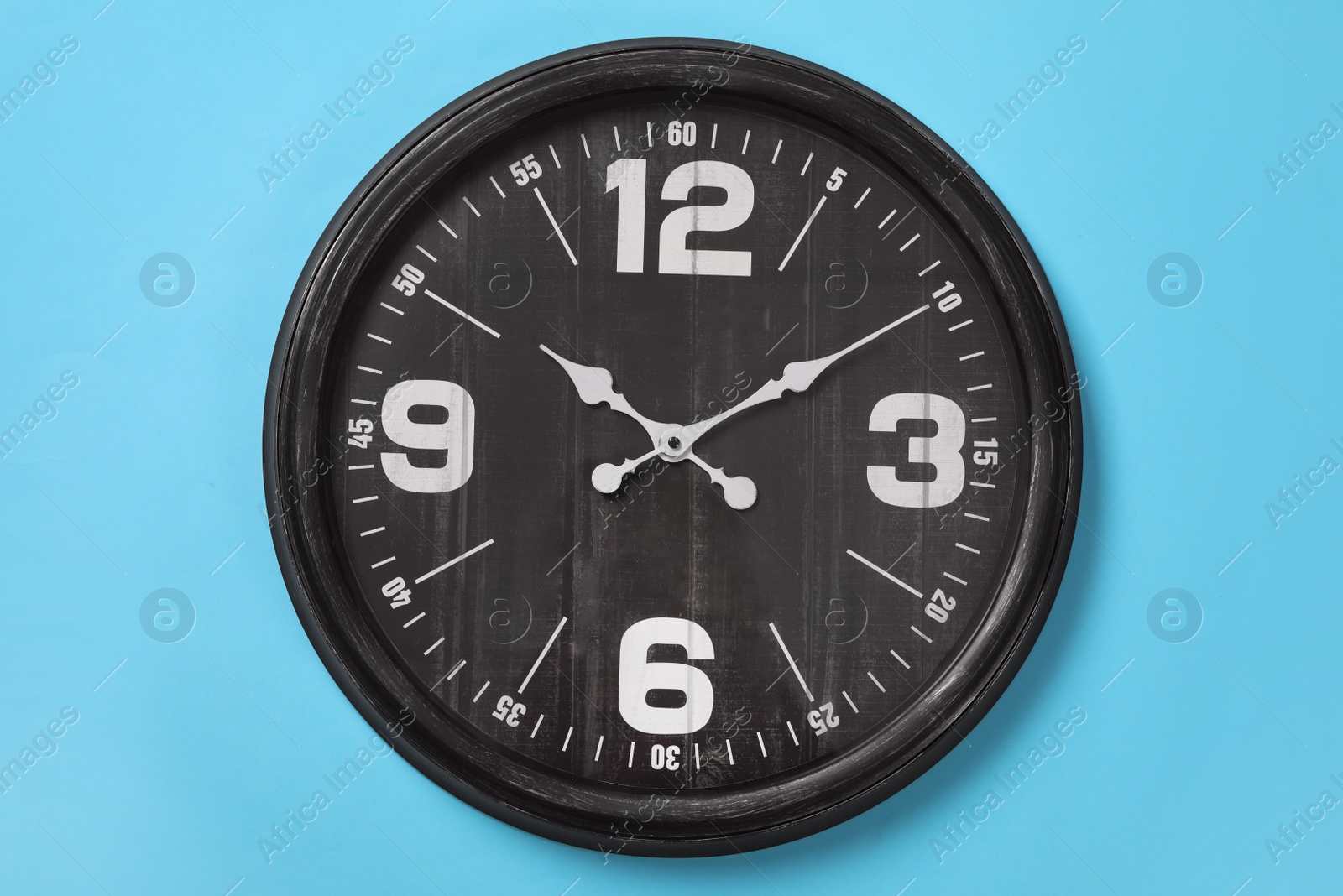 Photo of Stylish analog clock hanging on light blue wall