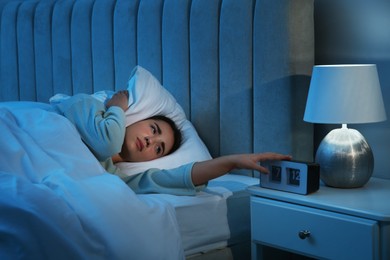 Photo of Unhappy young woman covering ears with pillow in bed at home. Noisy neighbours