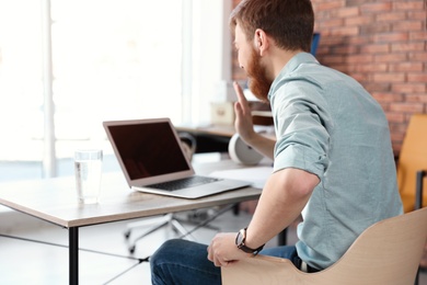 Young man using video chat on laptop in home office. Space for text