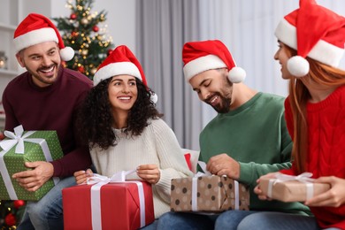 Photo of Christmas celebration in circle of friends. Happy woman and man opening gifts at home