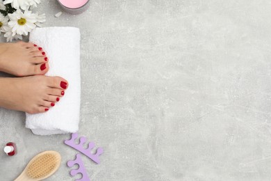 Photo of Woman with stylish red toenails after pedicure procedure, tools and chamomile flowers on grey textured background, top view. Space for text