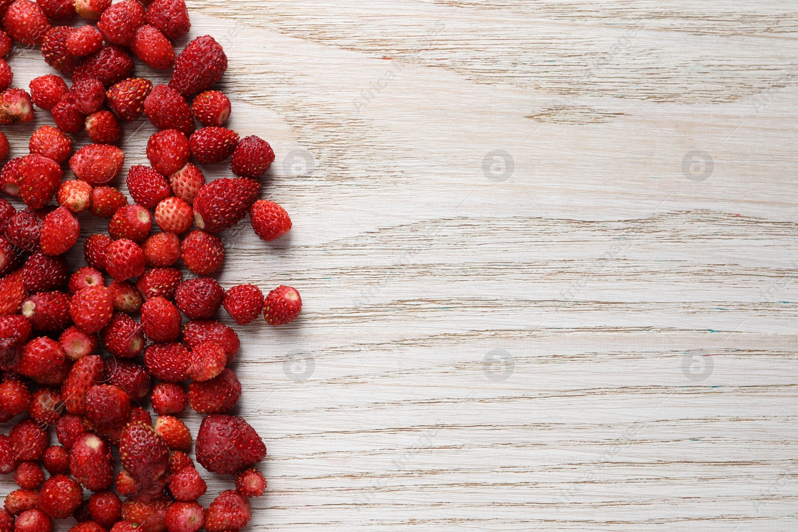 Photo of Many fresh wild strawberries on white wooden table, flat lay. Space for text